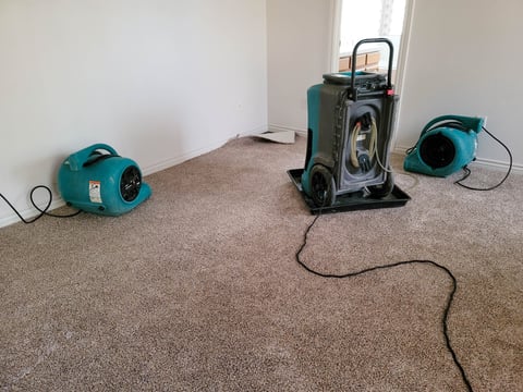 Two air movers and a dehumidifier drying a home after water damage.
