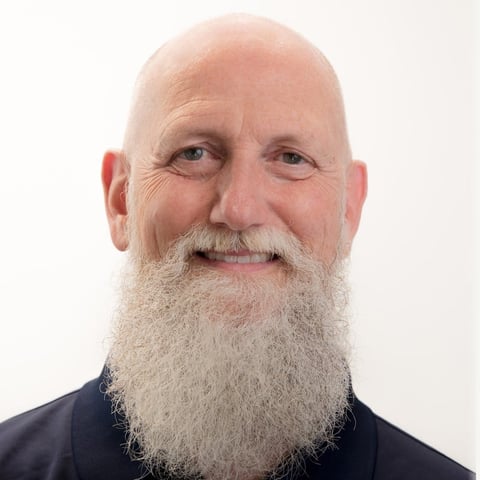 Bald man with long gray beard and mustache wearing dark shirt, smiling at camera against white background