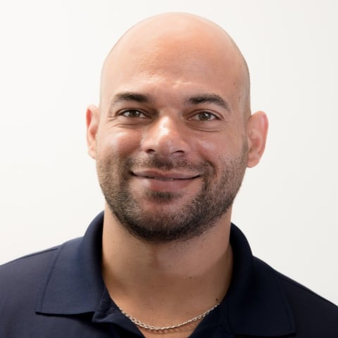 Portrait of a bald man with a beard wearing a dark navy polo shirt against a white background